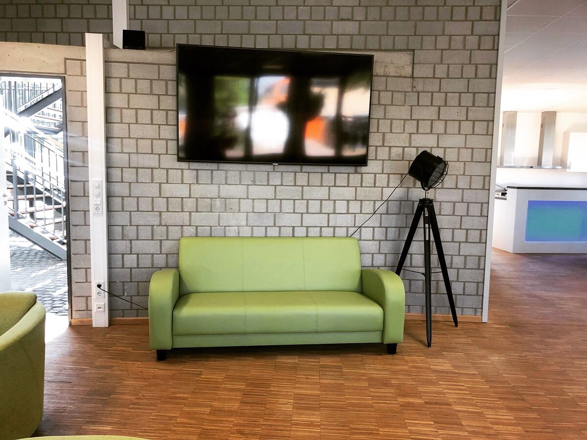 Ein hellgrünes Dreier-Sofa steht unter einem großen Flachbildschirm.